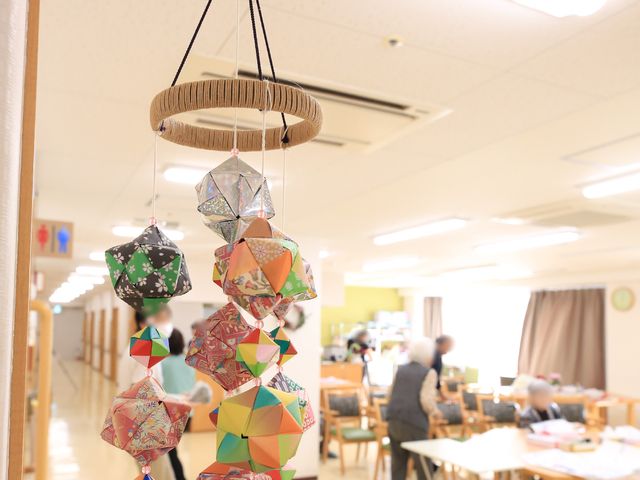 和風装飾のある廊下 掲示物 和紙で作られた飾りが廊下を彩り、そこを行き交う方たちが穏やかな日常を過ごされています。優しい雰囲気の中で、働く魅力が感じられます。