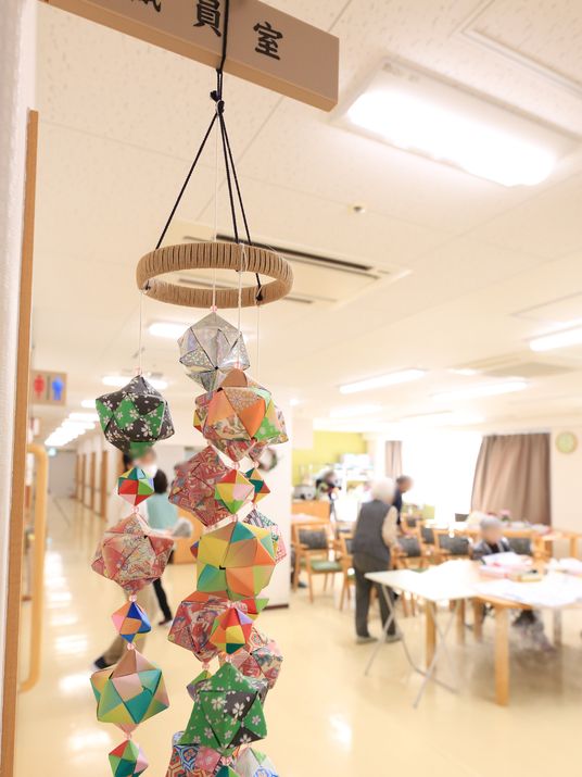談話室に隣接する職員室の看板の下に、手作りの手毬の飾りが吊るされている。色とりどりの和紙で作られている。
