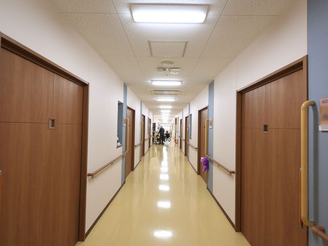 清潔な廊下 通路 手すりが設置された明るい廊下で、スタッフと住人が穏やかに会話を交わしています。安心してお仕事をする環境が整っています。